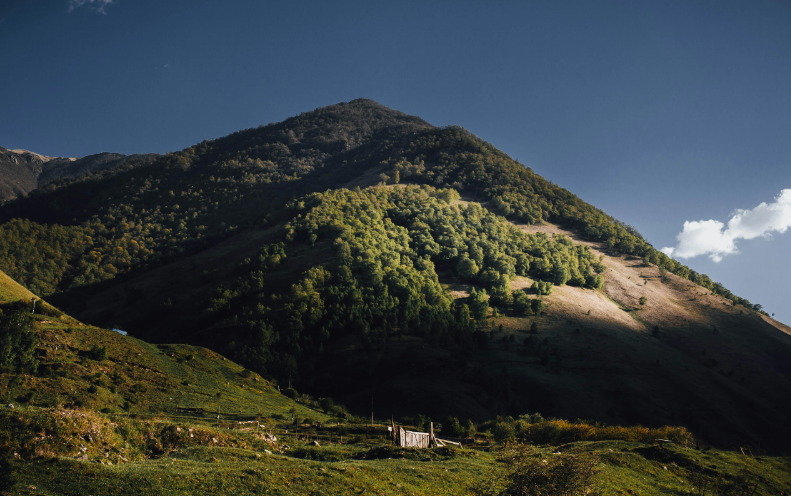 A scenic mountain with a quaint house perched on its summit, surrounded by clear blue skies.