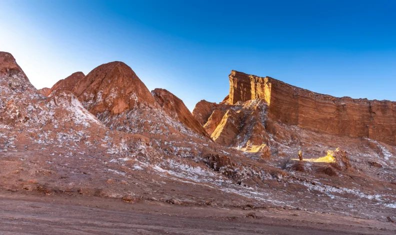 Sunset over desert mountains, casting warm hues of orange and purple across the rugged landscape.