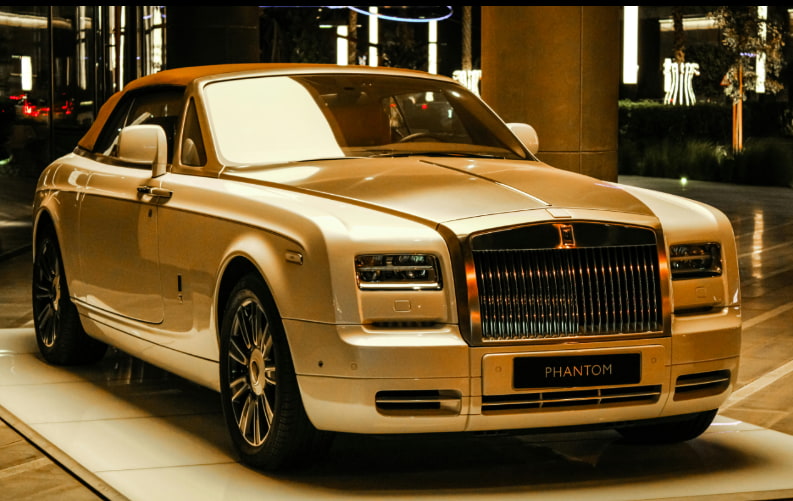 A Rolls Royce car parked in a spacious parking lot under clear blue skies.