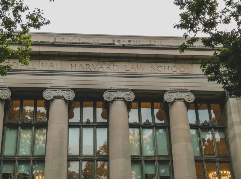 Harvard Law School building, a historic structure with classic architecture, surrounded by trees and a clear blue sky.