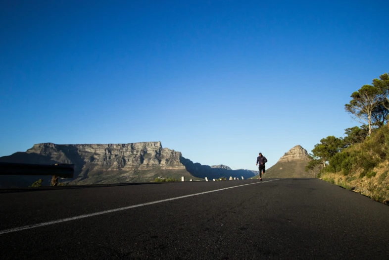 A person walks along a road with a mountain towering in the background.