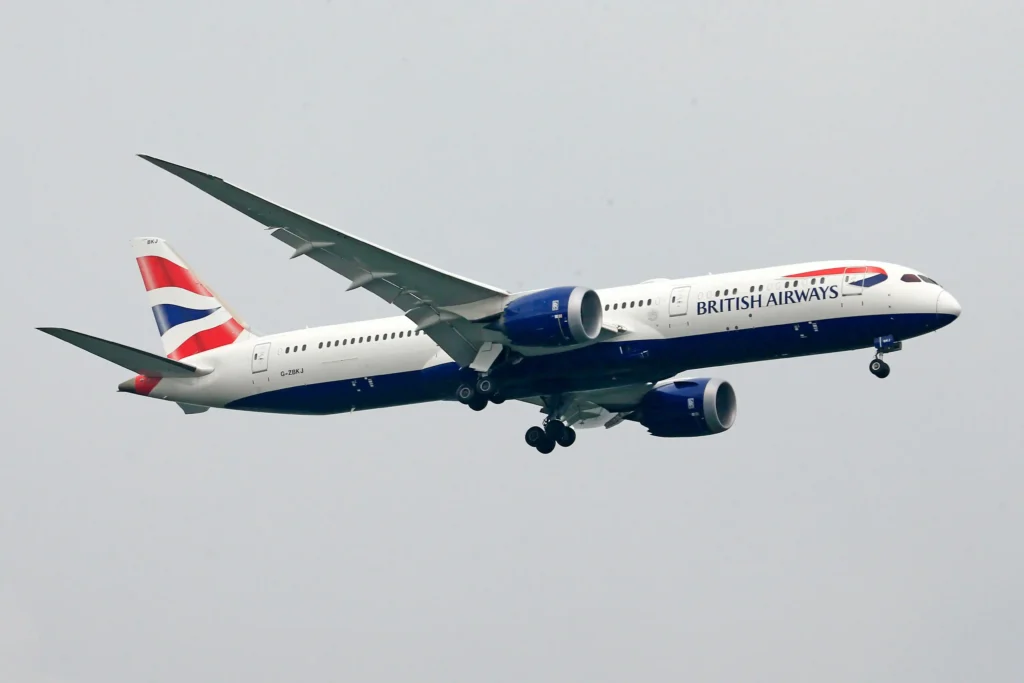 A British Airways plane soaring through a clear blue sky, showcasing its iconic livery against the backdrop of clouds.